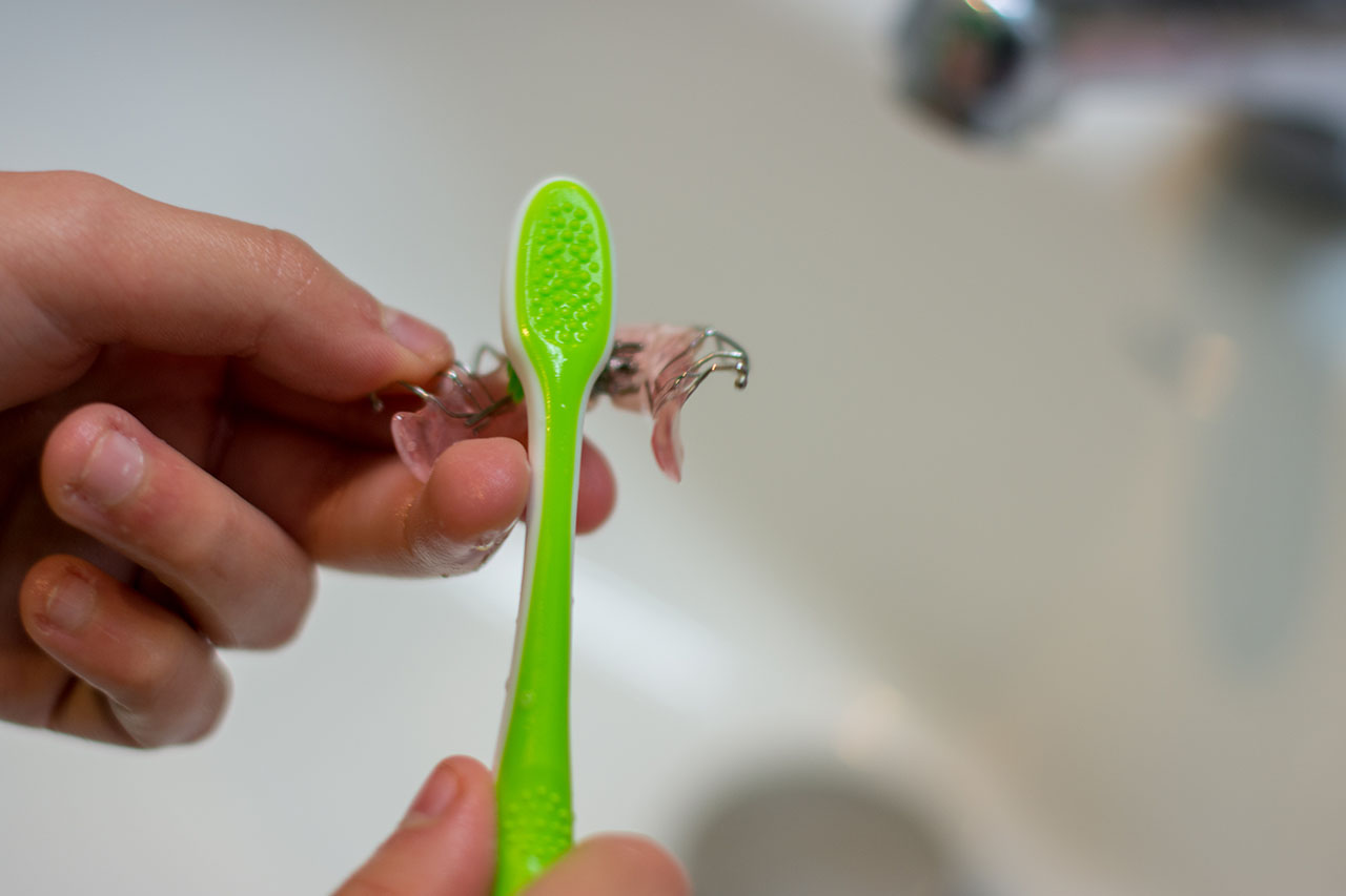 Cleaning a dental retainer with a toothbrush. Proper retainer care is essential after braces to maintain a straight smile.