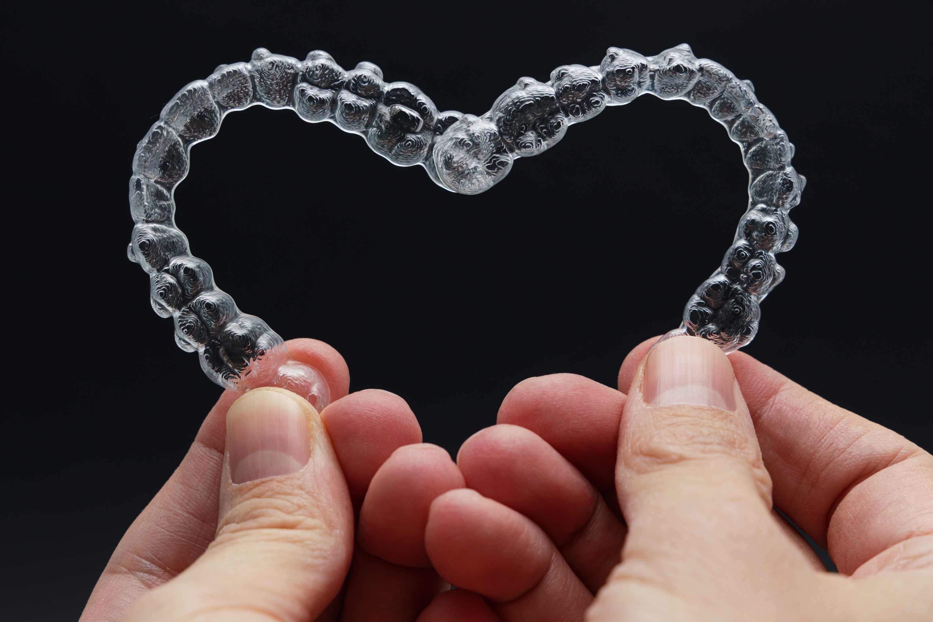 hands holding Invisalign clear aligners in shape of heart