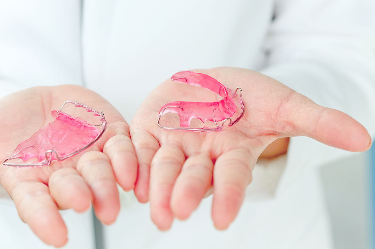 Orthodontist holding clear retainers after braces, ready to help patients maintain their perfect smiles.